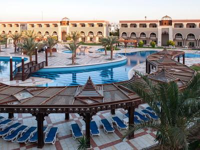 Gran área de piscina con tumbonas y sombrillas frente a un edificio de hotel al atardecer.