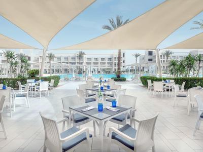 Terasa s bílými stoly a židlemi u bazénu v moderním hotelu.