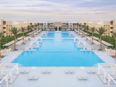 Großer blauer Swimmingpool mit weißen Liegestühlen und Palmen in einem modernen Hotelresort.