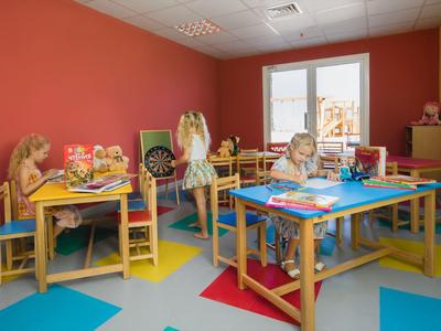 Děti si hrají v barevné místnosti s stolky a hračkami v hotelu.