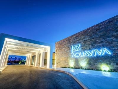 Moderní vstup do hotelu osvětlený v noci s osvětlenou cedulí na kamenné stěně.