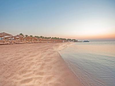 Weicher Sandstrand bei Sonnenuntergang mit ruhigem Meer und Strandbars im Hintergrund.
