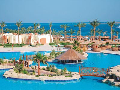 Großer Pool in tropischem Resort mit Palmen, Sonnenschirmen und Blick aufs Meer.