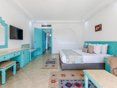 Lichte hotelkamer met turquoise meubels, tweepersoonsbed en tv aan de muur.