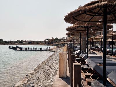 Budynek hotelu z basenem i palmami na pustynnym terenie pod bezchmurnym niebem.