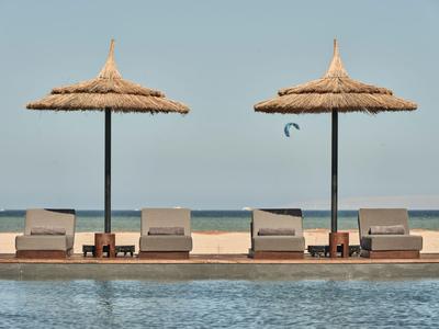Poolbereich mit Liegestühlen und Strohmachschirm am Strand