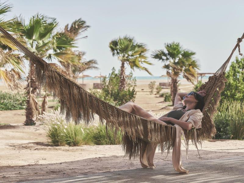 Woman relaxing in a hammock under palm trees in a dry landscape.
