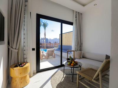 Lichte hotelkamer met grijze gordijnen, een klein tafeltje en schuifdeur naar buitenzitje.