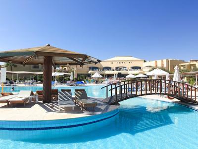 Großer Hotelpool mit Brücke, Sonnenschirmen und Liegestühlen unter klarem Himmel.