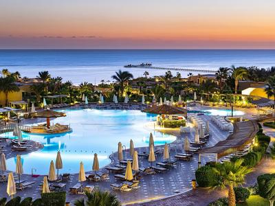 Großer Hotelpool bei Sonnenuntergang mit Liegen und Palmen am Meer.