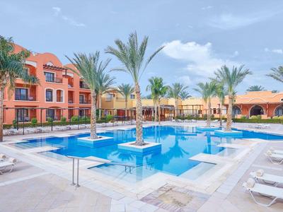 Moderní hotelový bazén s palmami a lehátky pod modrou oblohou.