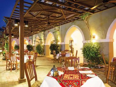 Pohodlná venkovní restaurace s prostřenými stoly a obloukovými okny při soumraku.