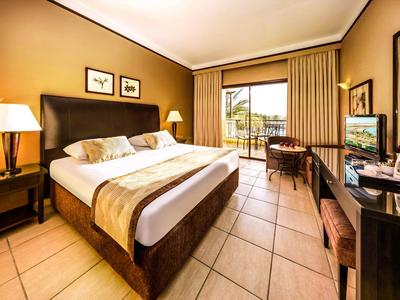 Gemütliches Hotelzimmer mit großem Bett, Schreibtisch und Blick auf Balkon mit Meer.