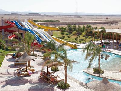 Blick auf einen Wasserpark mit Wasserrutschen und Pool, umgeben von Palmen und Liegestühlen.
