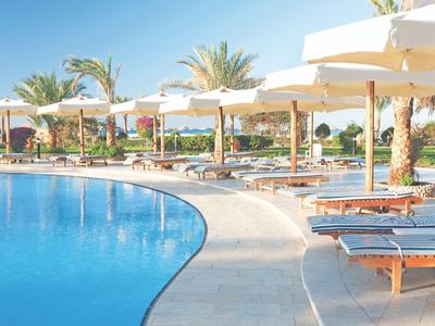 Piscina con tumbonas y sombrillas en un resort tropical en un día soleado.