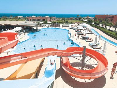 Gran piscina al aire libre con toboganes y sombrillas junto a un hotel cerca del mar.