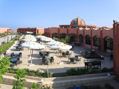 Área exterior de un hotel con mesas, sillas y sombrillas bajo un cielo despejado.