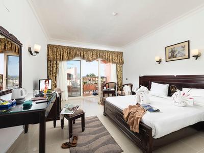 Bright hotel room with large bed, desk, mirror, balcony, and towels arranged on bed.