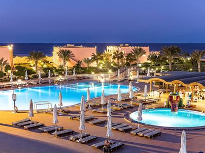 Piscina de hotel iluminada con tumbonas y jardín de palmeras por la noche junto al mar.