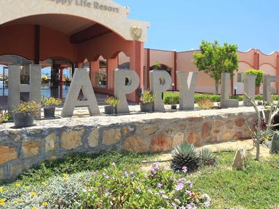 Large letters spelling 'Happy Inn' in front of a pink building with garden and blue sky.