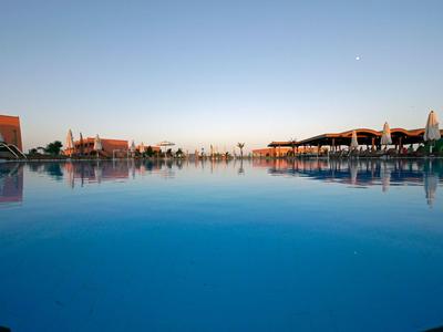 Gran piscina exterior con tumbonas y cielo azul claro al atardecer.
