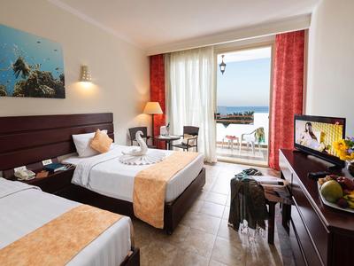 Habitación de hotel con dos camas, vista al mar desde el balcón e interior moderno en tonos cálidos.