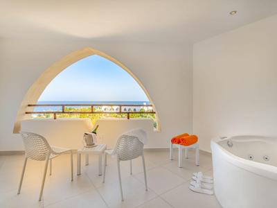 Helle Terrasse mit weißem Mobiliar, Blick auf Pool und Meer unter blauem Himmel.