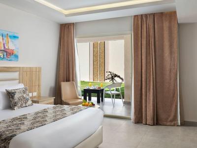 Camera d'hotel luminosa con letto matrimoniale e accesso a un balcone con divano.