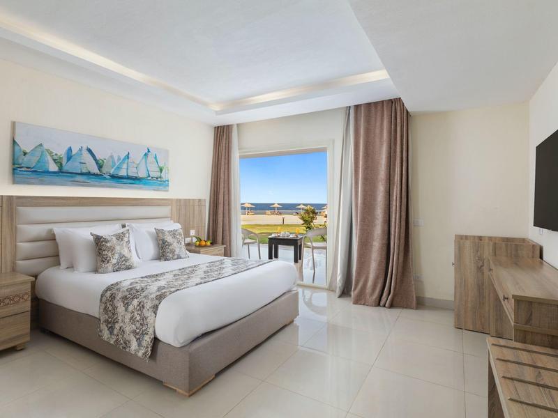 Camera d'hotel moderna con letto matrimoniale, TV a muro e vista su terrazza soleggiata.