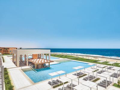 Moderner Poolbereich mit Liegestühlen und Blick auf das Meer bei klarem Himmel.