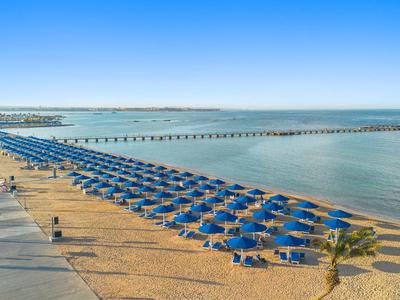 Strand met blauwe parasols en een boulevard aan zee bij heldere lucht.
