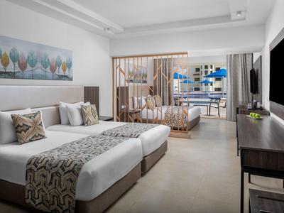 Moderne hotelkamer met twee bedden, zithoek en grote tv.