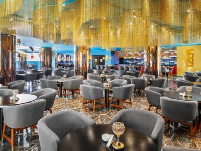 Moderne hotelinterieur met grijze fauteuils en gouden kroonluchters.