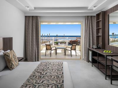 Modern hotelkamer met balkon en zeezicht, met bed, stoelen en bureau.