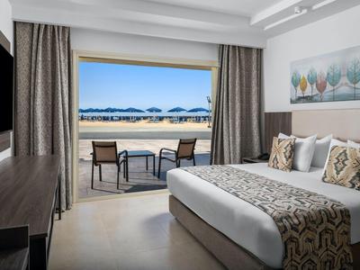 Hotelkamer met groot bed en terras met uitzicht op zee en parasols.