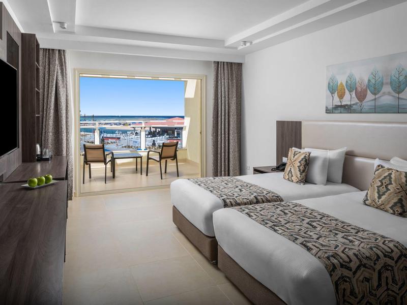 Modern hotelkamer met twee eenpersoonsbedden en balkon met zeezicht.