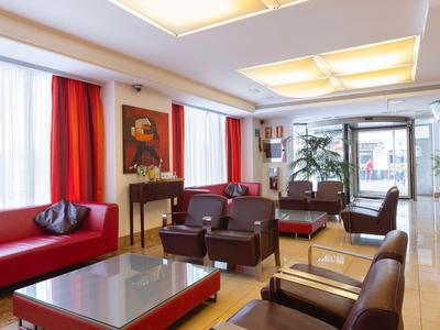 Helle Hotellobby mit roten Sofas, braunen Sesseln und großen Fenstern