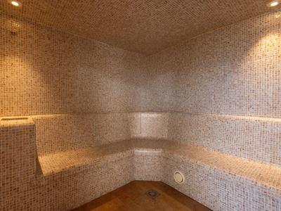 Kleiner Saunaraum mit Mosaikfliesen und integrierten Sitzbänken in L-Form unter warmer Beleuchtung.