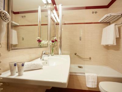 Hotel bathroom with beige tiles, white sink, bathtub, towel rack, and hair dryer.