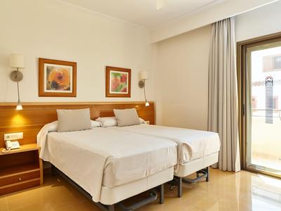 Hell eingerichtetes Hotelzimmer mit zwei Einzelbetten und Zugang zu einem Balkon.