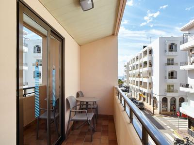 Balkon mit Stühlen und Tisch, Blick auf weiße Apartmentgebäude bei blauem Himmel.