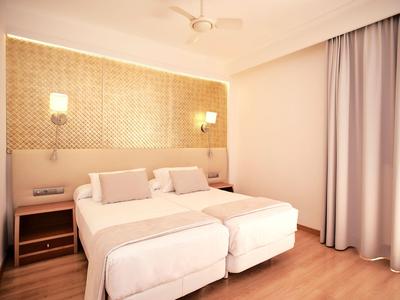 Helles Hotelzimmer mit zwei Einzelbetten, Nachttischen und Vorhängen.