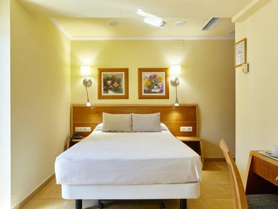 Schlichtes Hotelzimmer mit Doppelbett, zwei Bildern an der Wand und warmem Licht.