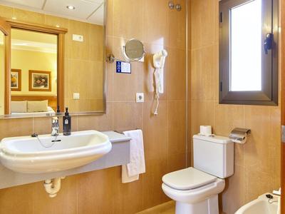 Helles Hotelbadezimmer mit Waschbecken, WC, Handtuch und Haartrockner an der Wand.