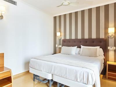 Hell eingerichtetes Hotelzimmer mit großem Doppelbett und gestreifter Akzentwand.