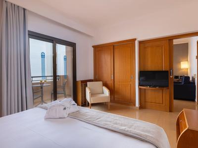 Helles Hotelzimmer mit Doppelbett, Sessel, TV, und Balkon mit Aussicht.