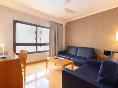 Gemütliches Hotelzimmer mit blauen Sofas, Holztisch und großem Fenster.