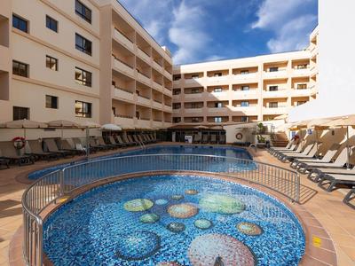 Innenhof eines Hotels mit Pool und mehreren Liegestühlen unter blauem Himmel.