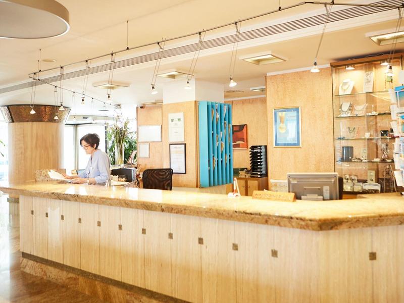 Hotel reception area with a wooden curved desk and a staff member working behind it.