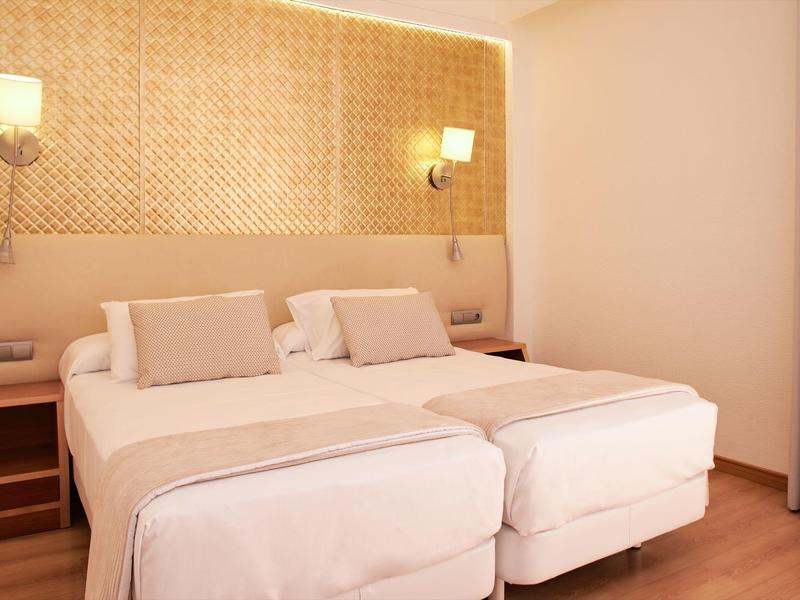Modern hotel room with twin beds, warm lighting, and wooden floors.